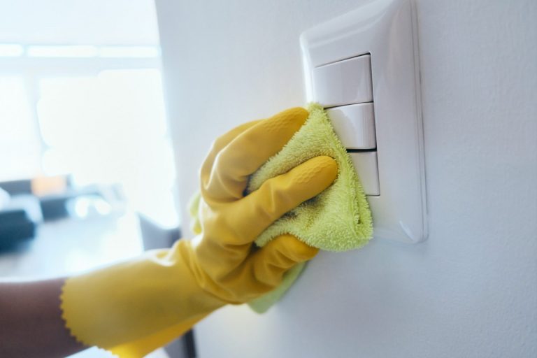 Gloved hand cleaning a light switch